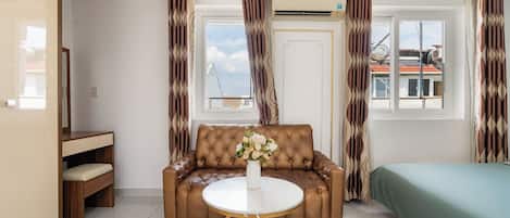 Un salon moderne avec un canapé en cuir marron, une table basse ronde et un lit recouvert d’une housse verte.