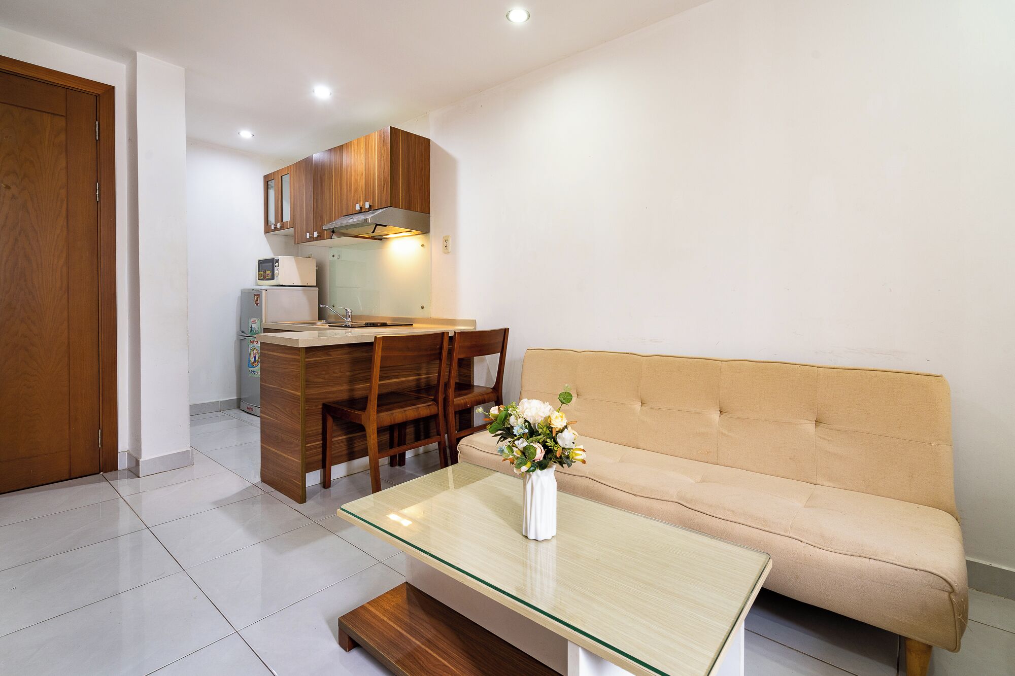 Un espacio habitable pequeño con kitchenette, un sofá, una mesa de centro de vidrio y una zona de comedor pequeña.