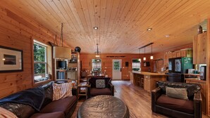 A cabin interior with a wooden ceiling, a sofa, a leather ottoman, a dining area, and a kitchen. - Lake Pend Oreille Escape HotTub, GameRoom & Views (Sagle)