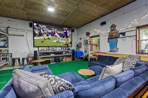 Habitació amb un televisor gran, sofàs blaus, un tir d'arc i un sostre de fusta.