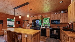 A wooden cabin-style kitchen with a central island, built-in appliances, and a large window. - Lake Pend Oreille Escape HotTub, GameRoom & Views (Sagle)