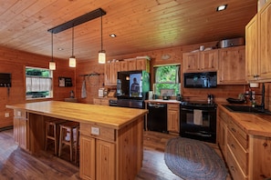 A wooden cabin-style kitchen with a central island, built-in appliances, and a large window.