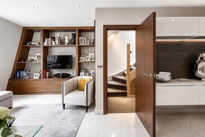 Ein modernes Wohnzimmer mit einer Couch, einem Fernseher und Holzregalen. Eine Treppe führt zu einer Küchenzeile.