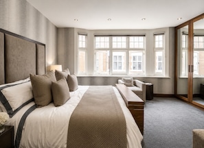 Ein modernes Schlafzimmer mit einem großen Bett, einer Bank, einem Sofa und einem Spiegel.