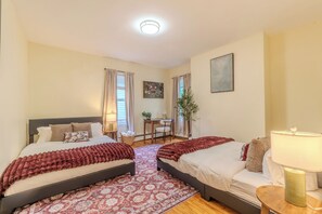 Quarto com duas camas, uma escrivaninha, uma cadeira, um abajur e uma planta.