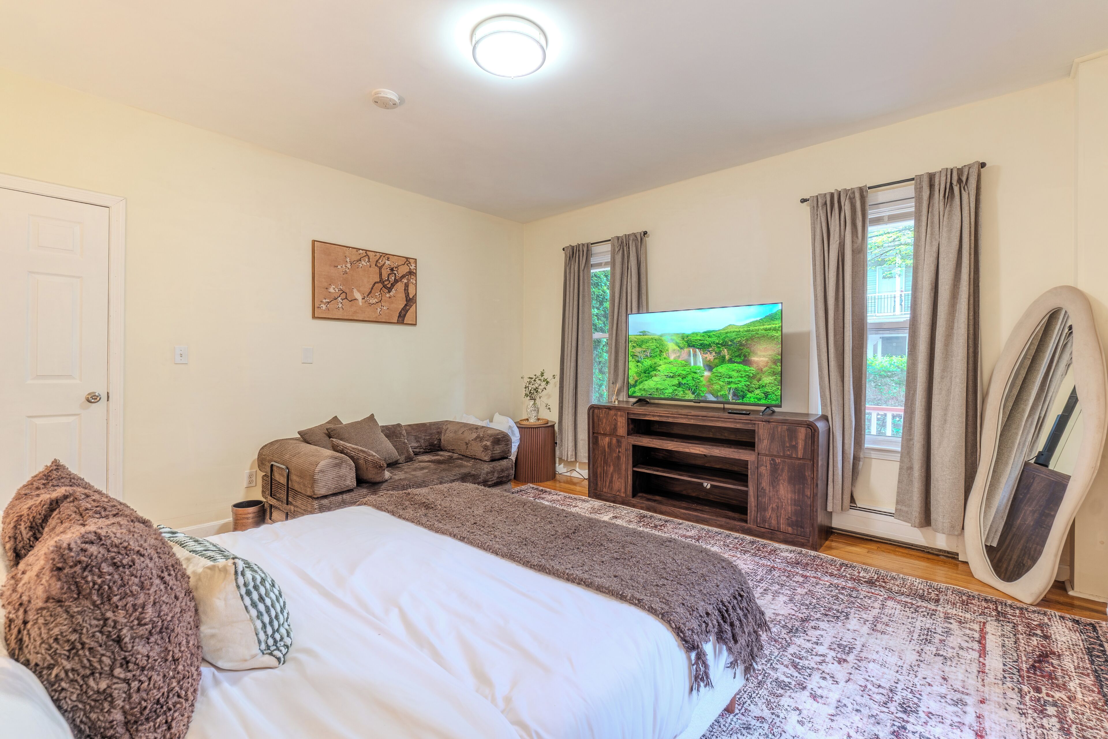 A bedroom with a bed, a television, a sofa, and a window with curtains.
