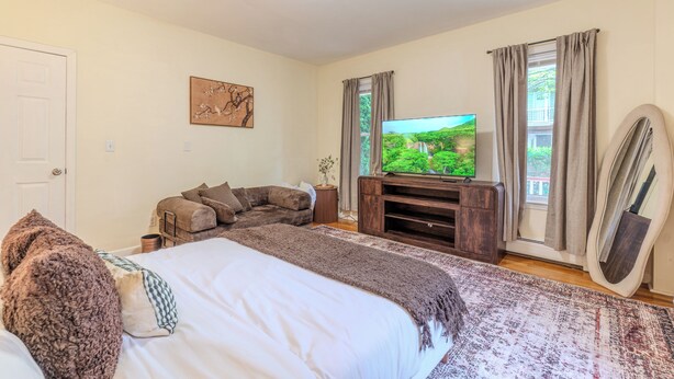 A bedroom with a bed, a television, a sofa, and a window with curtains. - Stylish Modern 5BR Home W/Private Balcony (Everett)