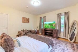 Quarto com cama, televisão, sofá e janela com cortinas.