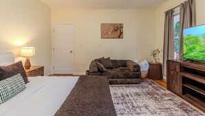 A bedroom with a bed, a sofa, a TV, and a door. - Stylish Modern 5BR Home W/Private Balcony (Everett)