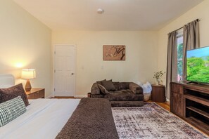 Quarto com cama, sofá, televisão e porta.