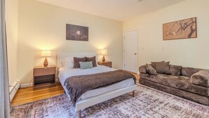 A bedroom with a bed, bedside tables, a sofa, a rug, and wall art. - Stylish Modern 5BR Home W/Private Balcony (Everett)