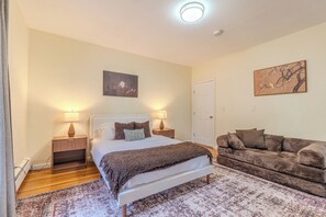 A bedroom with a bed, bedside tables, a couch, a rug, and artwork on the walls.