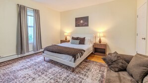 A bedroom with a bed, bedside lamps, a window with curtains, a rug, and a painting on the wall. - Stylish Modern 5BR Home W/Private Balcony (Everett)