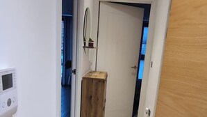 A hallway with wooden flooring, a door on the right, and a wall-mounted thermostat on the left. - Cosy Retreat in Gloucester (Gloucester)
