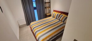 Ein Schlafzimmer mit Bett, einem Fenster mit Vorhängen, einem Heizkörper und einem Holzbodenbrett.