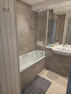 Ein modernes Badezimmer mit einer gläsernen Duschkabine, einer Badewanne, einem Waschtisch und einem Spiegel.