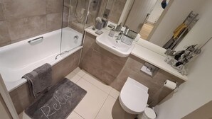 A modern bathroom with a bathtub, a sink, a toilet, and a shower area. - Cosy Retreat in Gloucester (Gloucester)