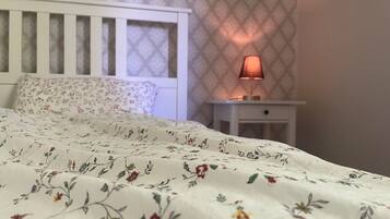 Un dormitorio con colcha estampada, cabecera blanca, mesita de noche con lámpara y papel tapiz decorado.
