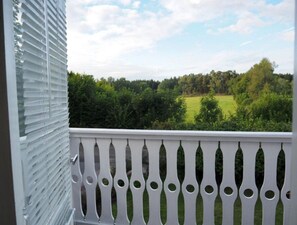 Ein Balkon mit weißer Brüstung und Blick auf eine grüne Landschaft.