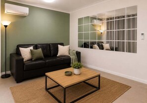 Ein Wohnzimmer mit einem schwarzen Ledersofa, einem Holztisch, einer Stehlampe und einem großen Spiegel an der Wand.
