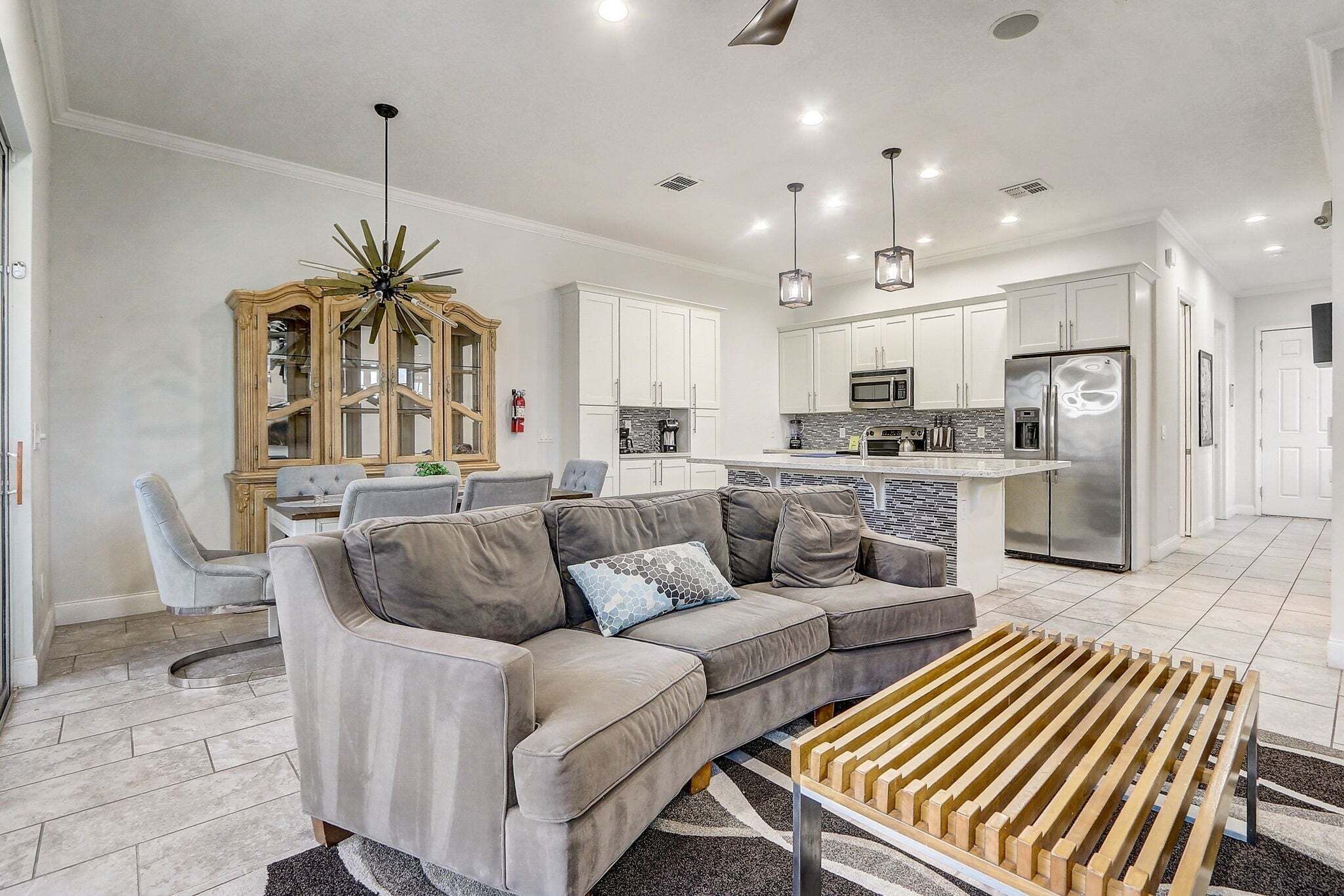 A modern kitchen with white cabinets, stainless steel appliances, and a dining area with a gray sofa and a wooden coffee table.