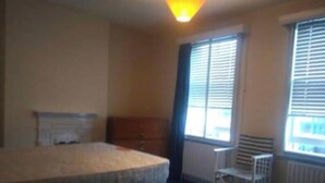 Ein Schlafzimmer mit Bett, Heizkörper, einem Fenster mit Jalousien und einem Sessel.