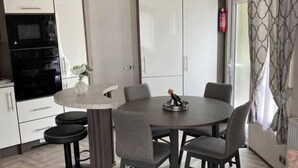 A compact kitchen with a microwave, oven, and cabinets, a dining area with a round table and chairs, and a sofa.