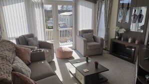 A living room with a sofa, armchair, ottoman, coffee table, fireplace, and a view of the outside.