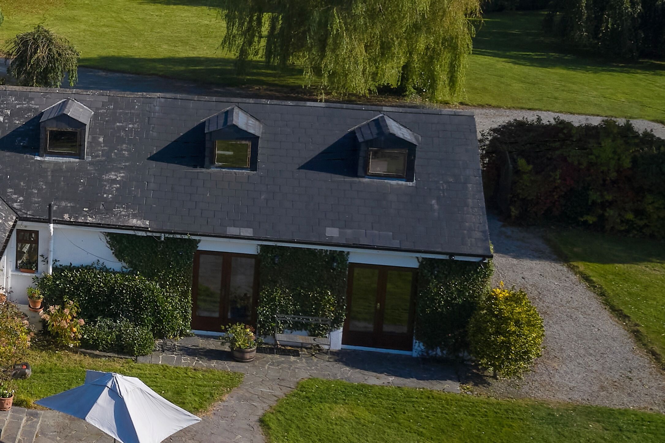 Une maison à deux étages, dotée d’un toit en pente, d’un porche à l’avant et d’un petit jardin.