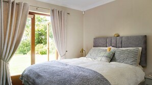 Een slaapkamer met een bed, gordijnen, een nachtkastje en uitzicht door een glazen deur.