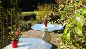 Een tuin met twee tafels met glazen blad, omgeven door groen en een houten hek.
