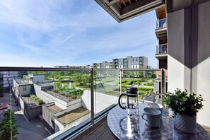 A balcony with a view of a green park, a metal table with a coffee pot, and a potted plant. - 1-bedroom Apartment Central Milton Keynes Amethyst House (Moffat)