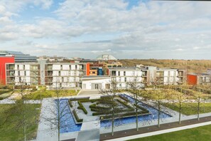 A modern building complex with multiple structures, a central courtyard with a water feature, and a surrounding landscaped area. - 1-bedroom Apartment Central Milton Keynes Emerald House (Moffat)