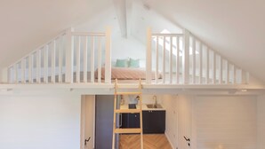 A loft bedroom with a bunk bed, a wooden ladder, a kitchen area, and a bathroom.