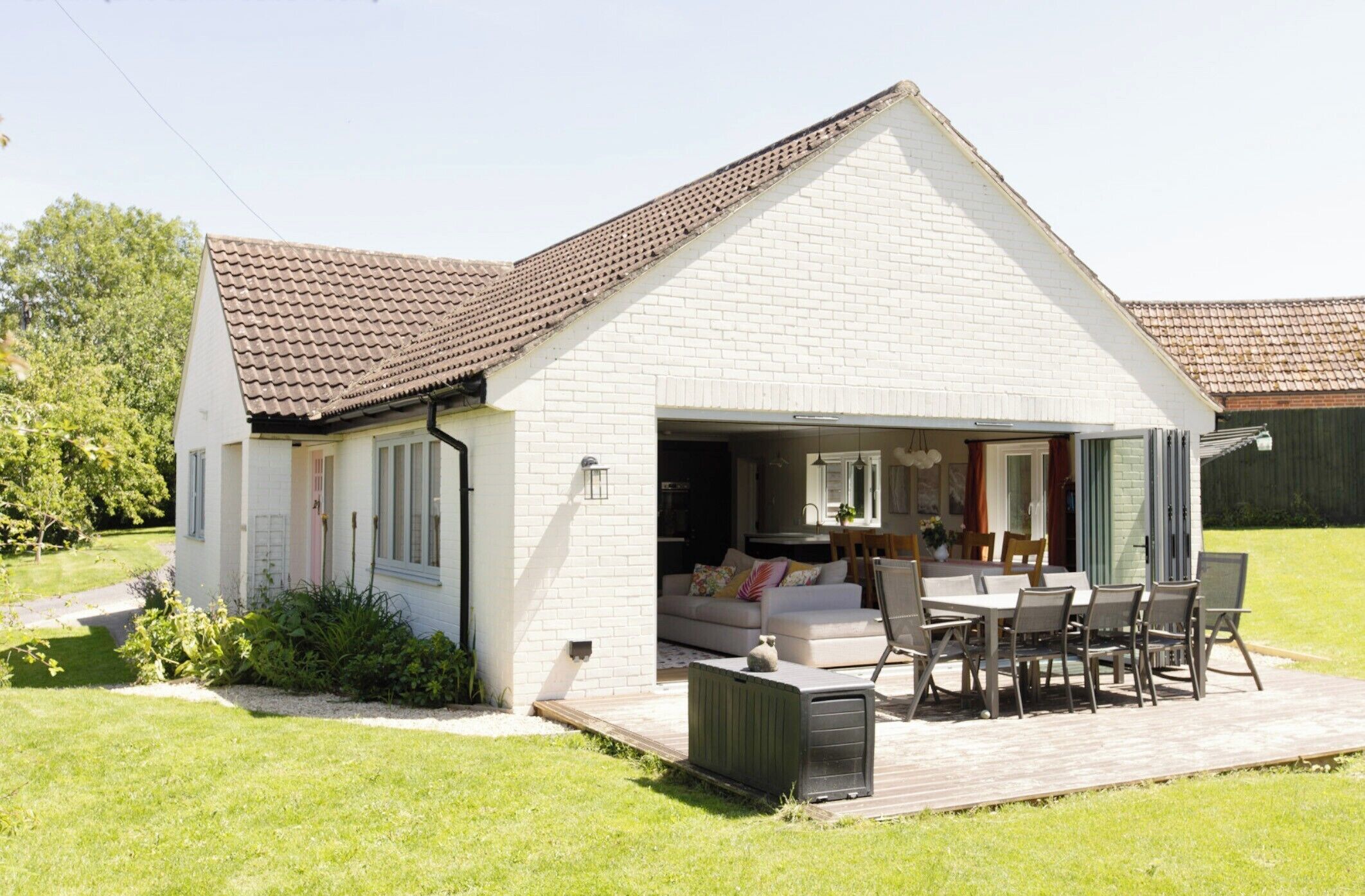 A small, single-story house with a patio area, a sofa, and a dining table set outside.