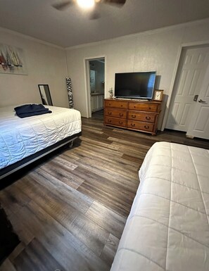 Ein Schlafzimmer mit zwei Betten, einer Holzkommode, einem Fernseher und einer Tür.