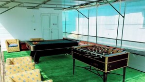 Una habitación con mesa de fútbol, césped artificial verde y sillas amarillas con estampado.