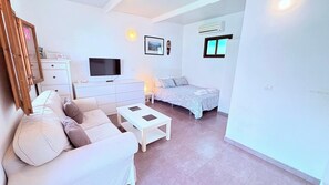 Ein modernes Wohnzimmer mit Sofa, Fernseher, Bett mit gemustertem Überwurf und einem kleinen Tisch.