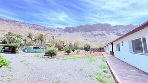 Zona residencial con un edificio blanco, un patio de grava y montañas al fondo.