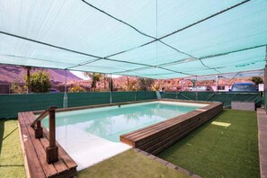 A swimming pool with a wooden deck and a green netted roof. - Tiny House in the Country (San Bartolome de Tirajana)