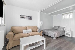 A room with a beige sofa, a white coffee table, a bed with a patterned bedspread, a white nightstand, and a wall-mounted fan. - Tiny House in the Country (San Bartolome de Tirajana)