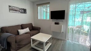 A living room with a brown sofa, a white coffee table, a flat-screen TV mounted on the wall, and a window with a view of the outside. - Renovated Tiny House (San Bartolome de Tirajana)