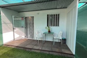 Eine überdachte Terrasse mit einer Schiebetür, einem kleinen Tisch mit Stühlen und einem Blumentopf.