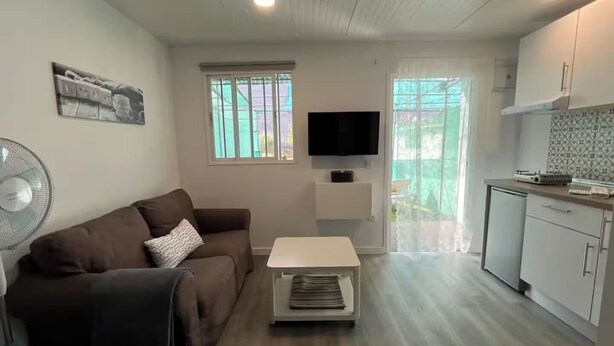 A compact living space with a sofa, a small table, a TV, and a kitchenette. - Renovated Tiny House (San Bartolome de Tirajana)