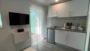 A modern kitchen with white cabinets, a built-in oven, a sink, and a television mounted on the wall. - Renovated Tiny House (San Bartolome de Tirajana)