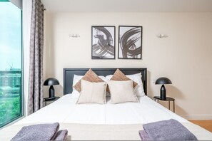 A hotel room with a large bed, two bedside tables, a window with curtains, and abstract art on the wall. - Riverside 1-bed Apt w Balcony in Vauxhall Zone 1 (London)