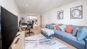 A modern living room with a sofa, a TV, and a dining area. - Riverside 1-bed Apt w Balcony in Vauxhall Zone 1 (London)