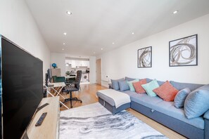A modern living room with a sofa, a TV, and a dining area. - Riverside 1-bed Apt w Balcony in Vauxhall Zone 1 (London)