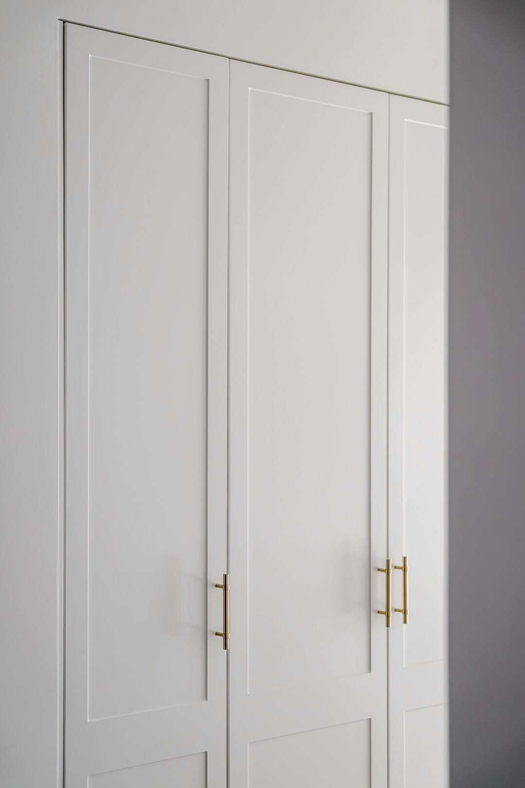 A white wardrobe with two doors and gold handles.