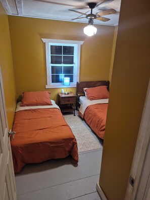Un dormitorio con dos camas, una mesita de noche, una lámpara, un ventilador de techo y una ventana.